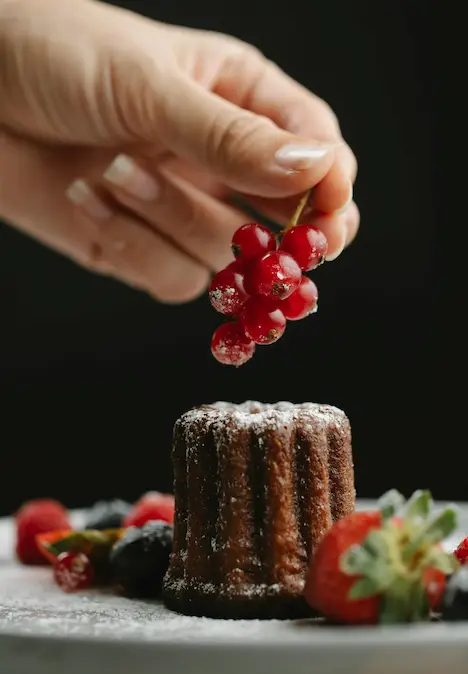 A person puts grapes on a cupcake